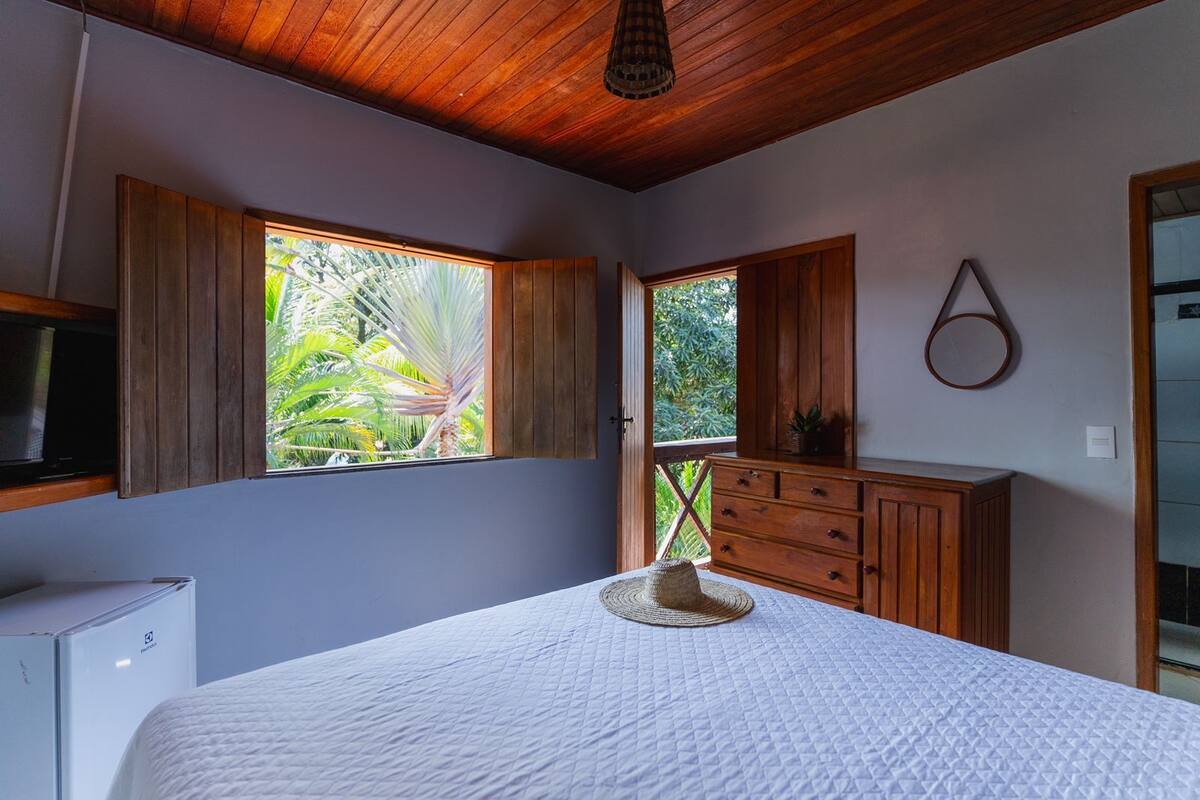 Une chambre à coucher avec un lit, une armoire en bois et une fenêtre donnant sur un paysage verdoyant.