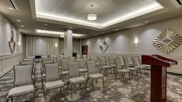 Una sala conferenze con file di sedie, un podio e una moquette decorata.