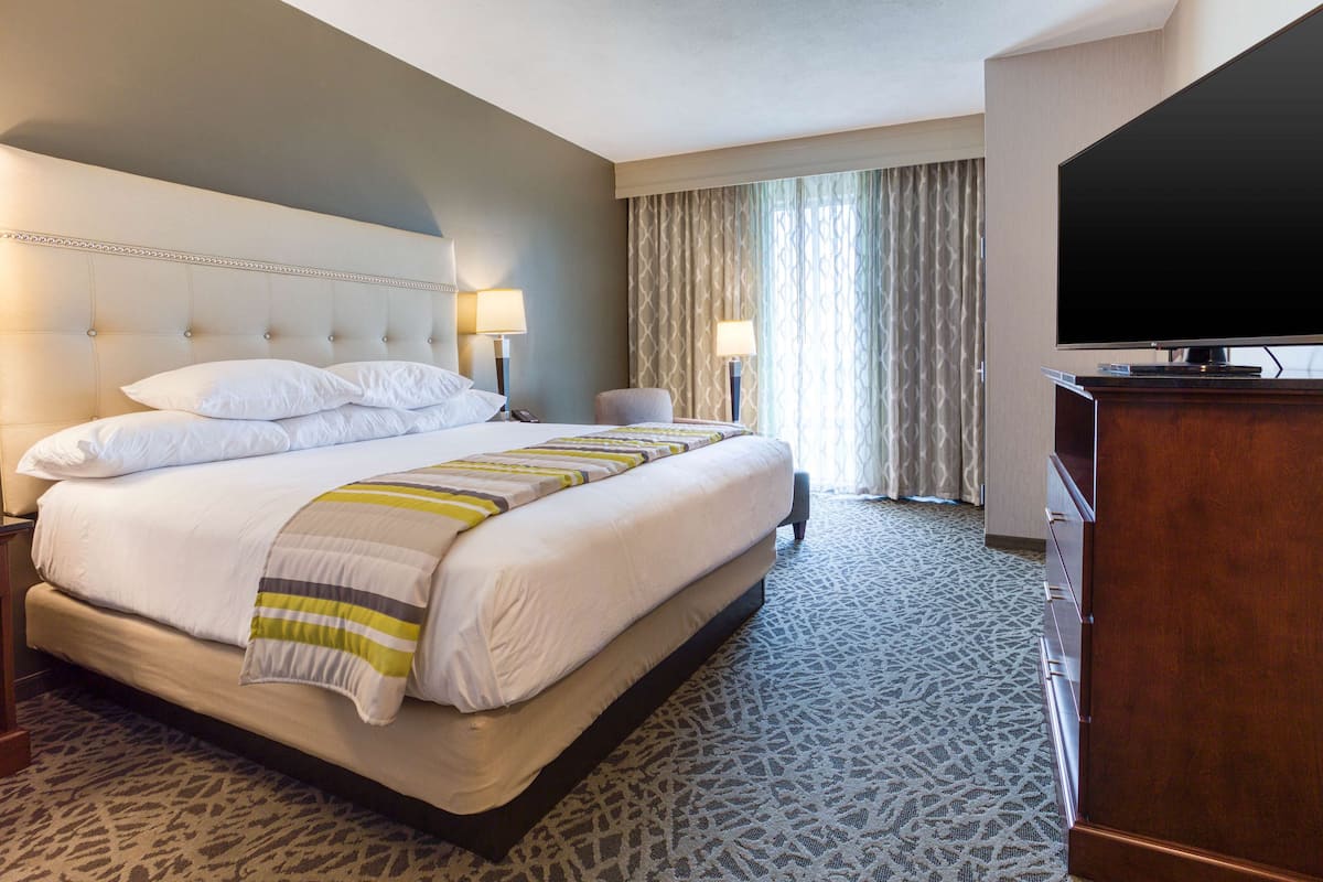 A hotel room with a large bed, two bedside lamps, a television, and a wooden dresser.