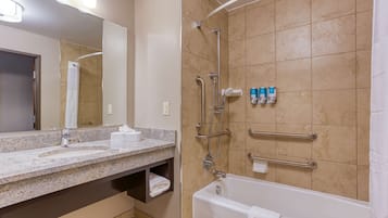 Un baño moderno con encimera de granito, bañera, ducha con barras de apoyo y espejo.