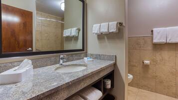 A bathroom with a granite countertop sink, a mirror, and a toilet. There are towels hanging on the wall and a trash can.