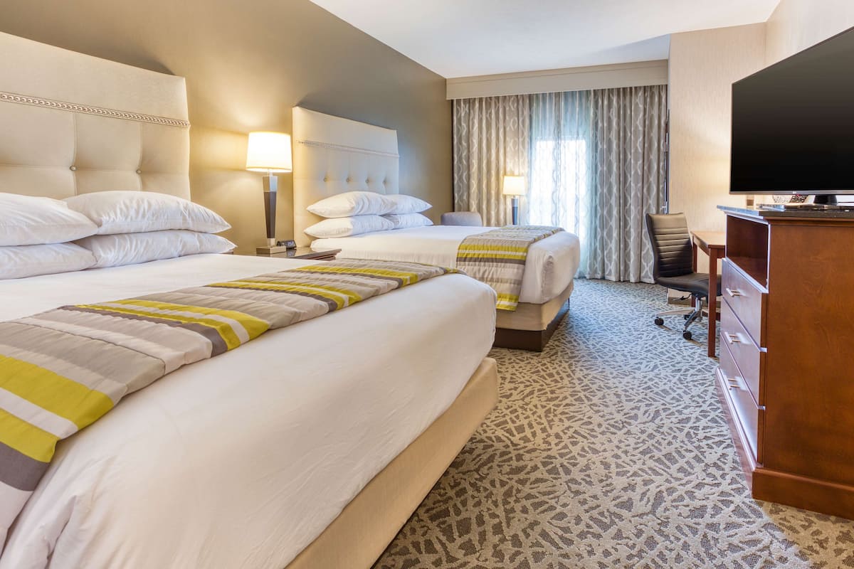A hotel room with two beds, a TV, a desk, and a chair.