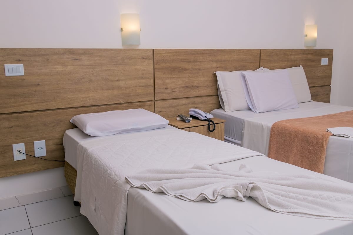 A hotel room with two beds, a wooden headboard, bedside tables, and wall-mounted lights.