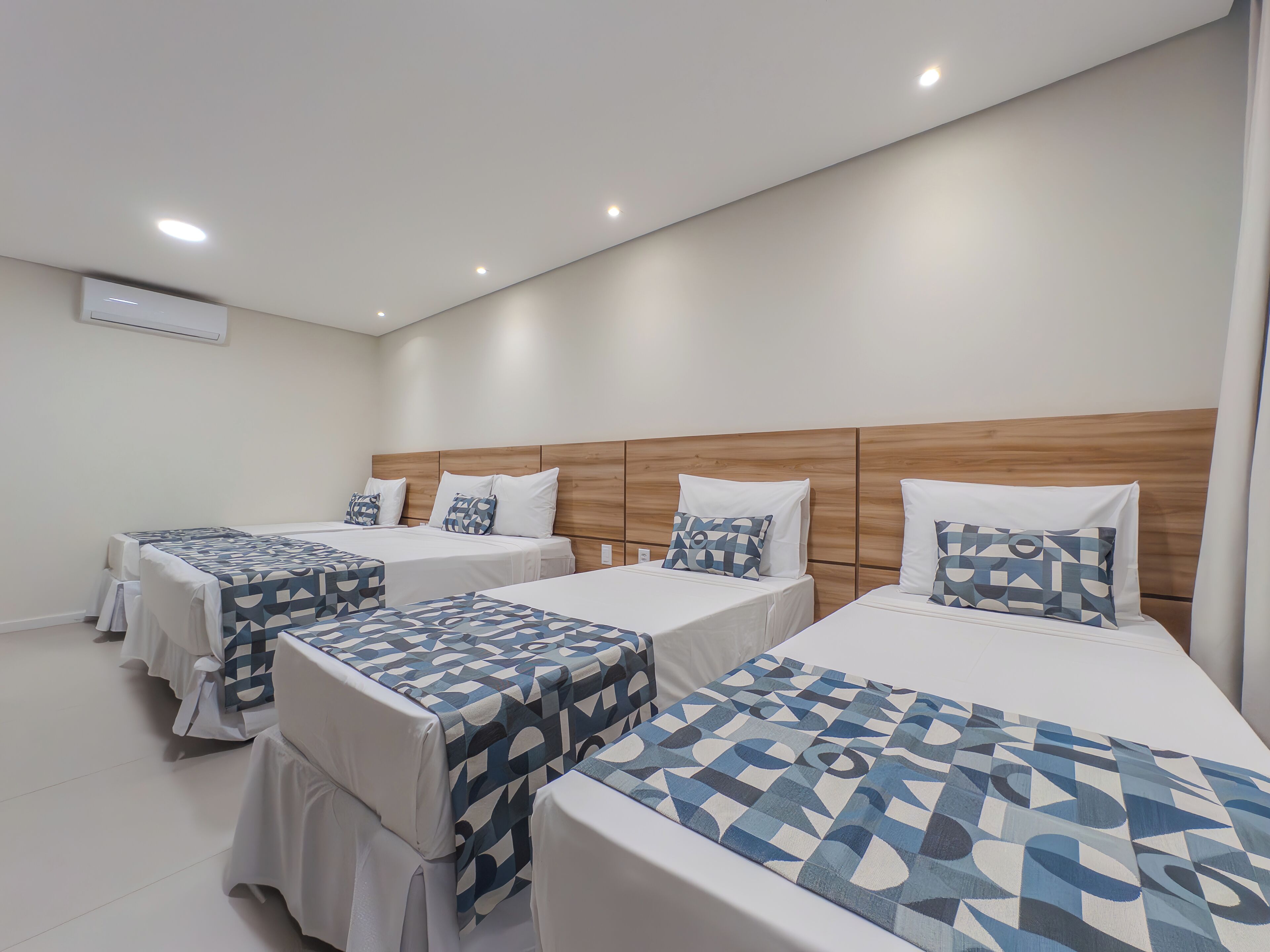 A hotel room with three beds, each with a geometric-patterned bedspread and white pillows.