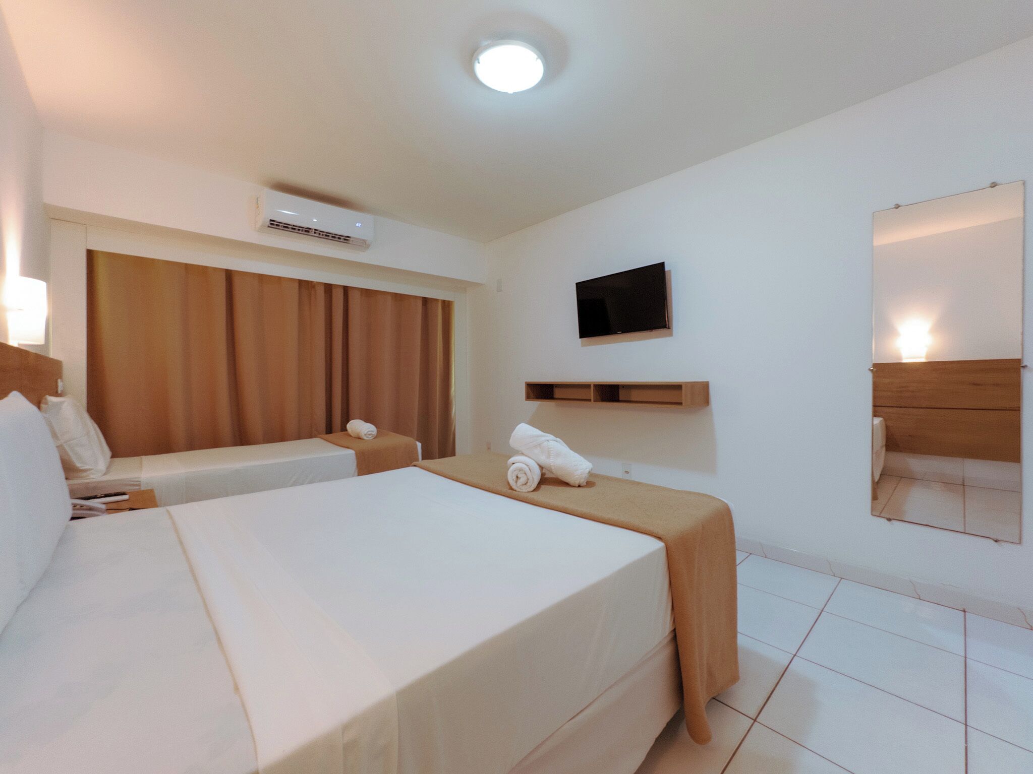 A hotel room with a large bed, a bedside table, a TV, and a ceiling-mounted air conditioner.