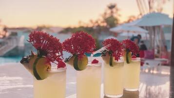 Three glasses of a yellow beverage with red flowers and lime slices on a reflective surface.