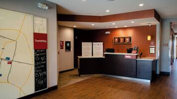 A hotel reception area with a reception desk, a map on the wall, and a sign with a date and temperature.