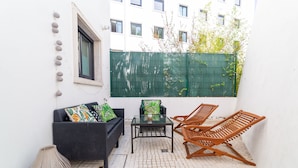 A small patio with a sofa, two chairs, a table, and a decorative vase.