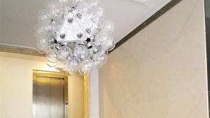 A staircase with a modern chandelier and a metallic elevator in the background.
