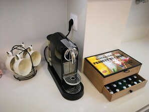 Une machine à café, un ensemble de tasses et une boîte de sachets de thé Lipton sont posés sur un plan de travail.