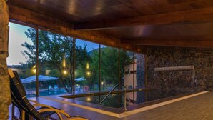 Una habitación moderna con un gran muro de vidrio, un banco de madera y una chimenea de piedra.