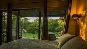 Un dormitorio con una cama grande, vistas a un jardín y un balcón con mesa y sillas.
