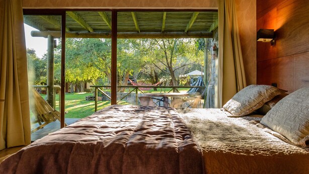 Un dormitorio con una cama grande, vista al jardín y techo de madera.