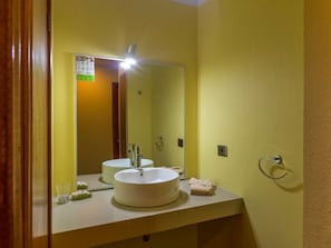 Un baño con un lavamanos redondo, un espejo y un toallero.