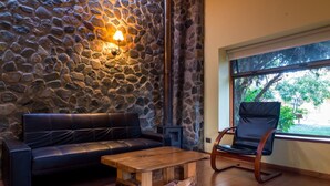 Una pared de piedra con chimenea empotrada, un sofá de cuero, una mesa de centro de madera y un sillón mecedor en una habitación con un ventanal grande.