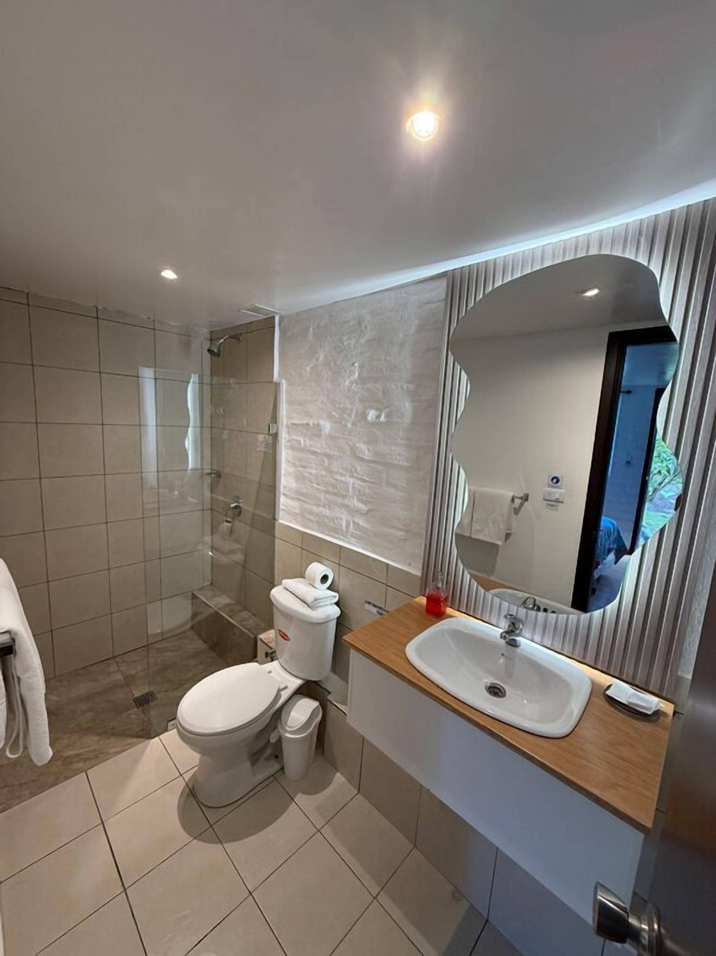A modern bathroom with a glass-enclosed shower, a toilet, a sink with a mirror, and a towel rack.
