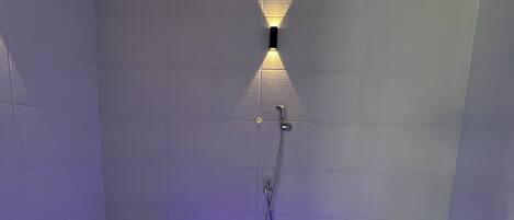 A modern shower room with a built-in bench, a handheld showerhead, and a wall-mounted light fixture.