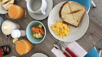 A breakfast table with scrambled eggs, toast, fruit, and juice.