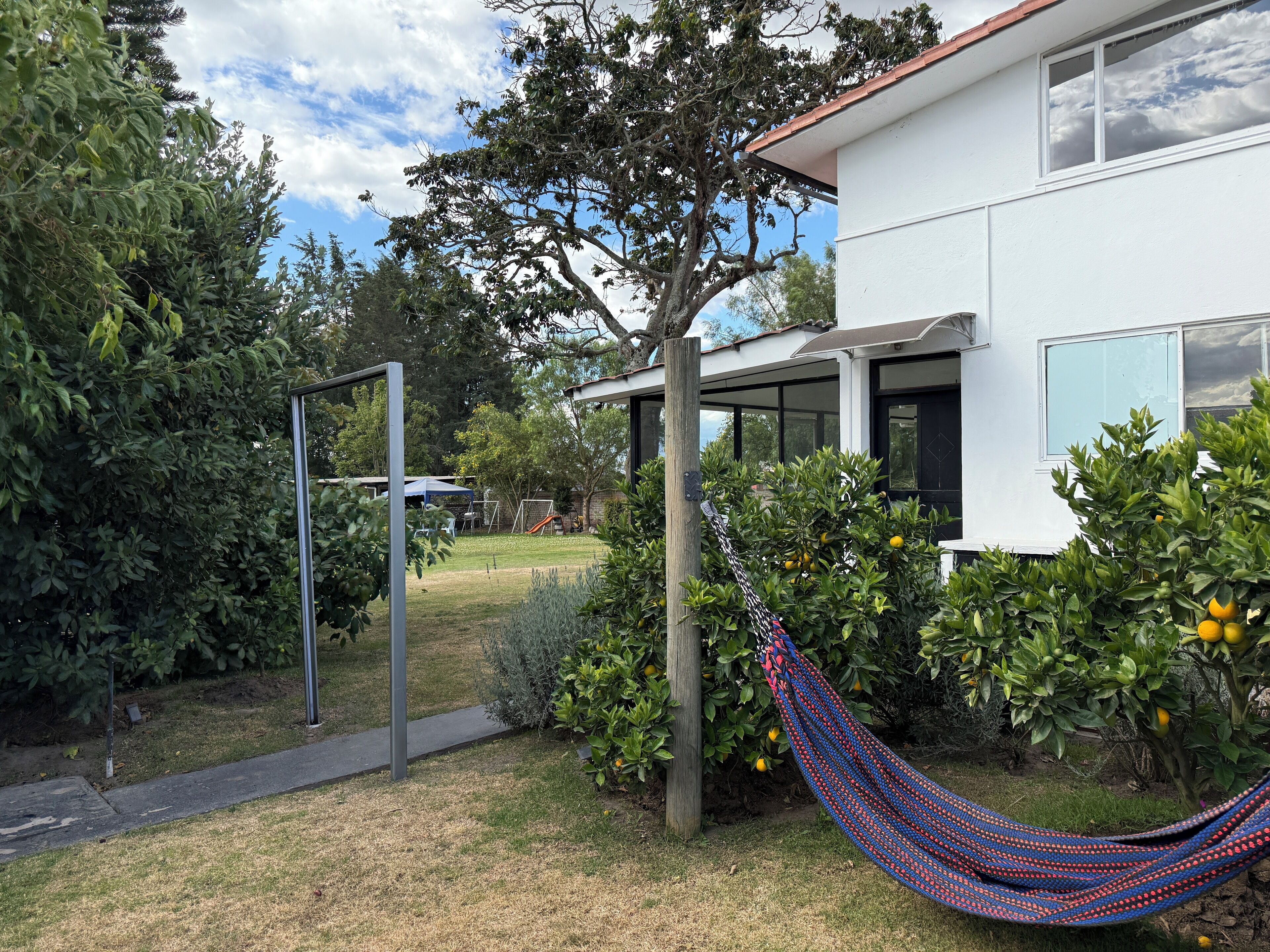 Ein modernes Haus mit weißer Fassade, einer Hängematte und einem Garten mit Bäumen und einem Fußballtor.