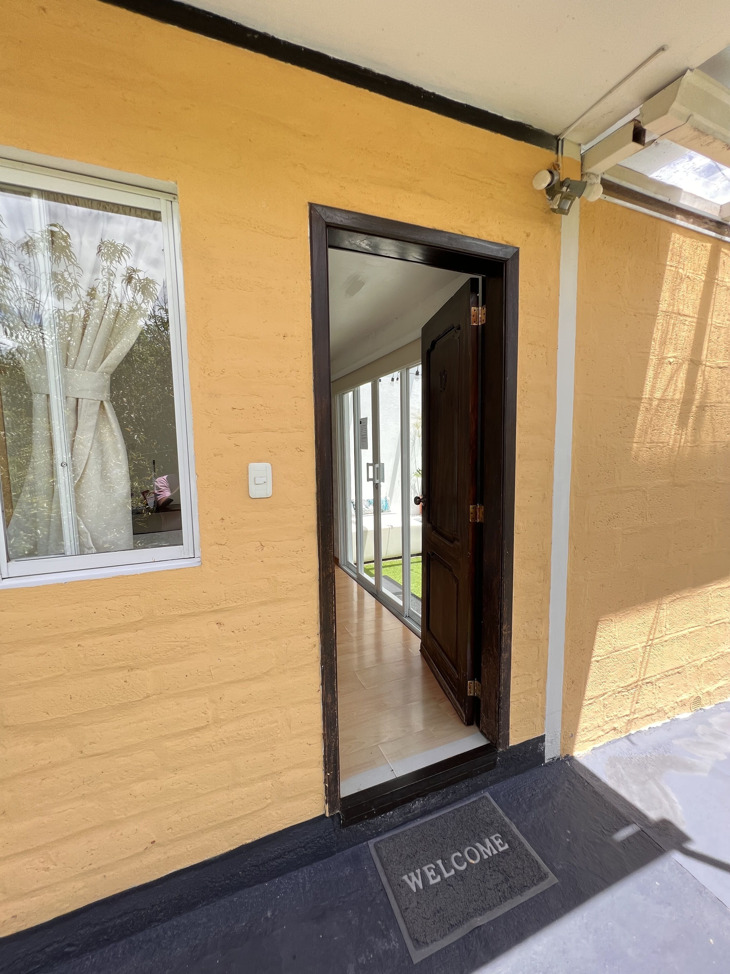 L’entrée d’un hôtel, avec une porte en bois, un paillasson et une fenêtre avec un rideau.