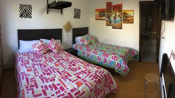 A room with two beds, each with patterned bedding, a small stool, and wall art.