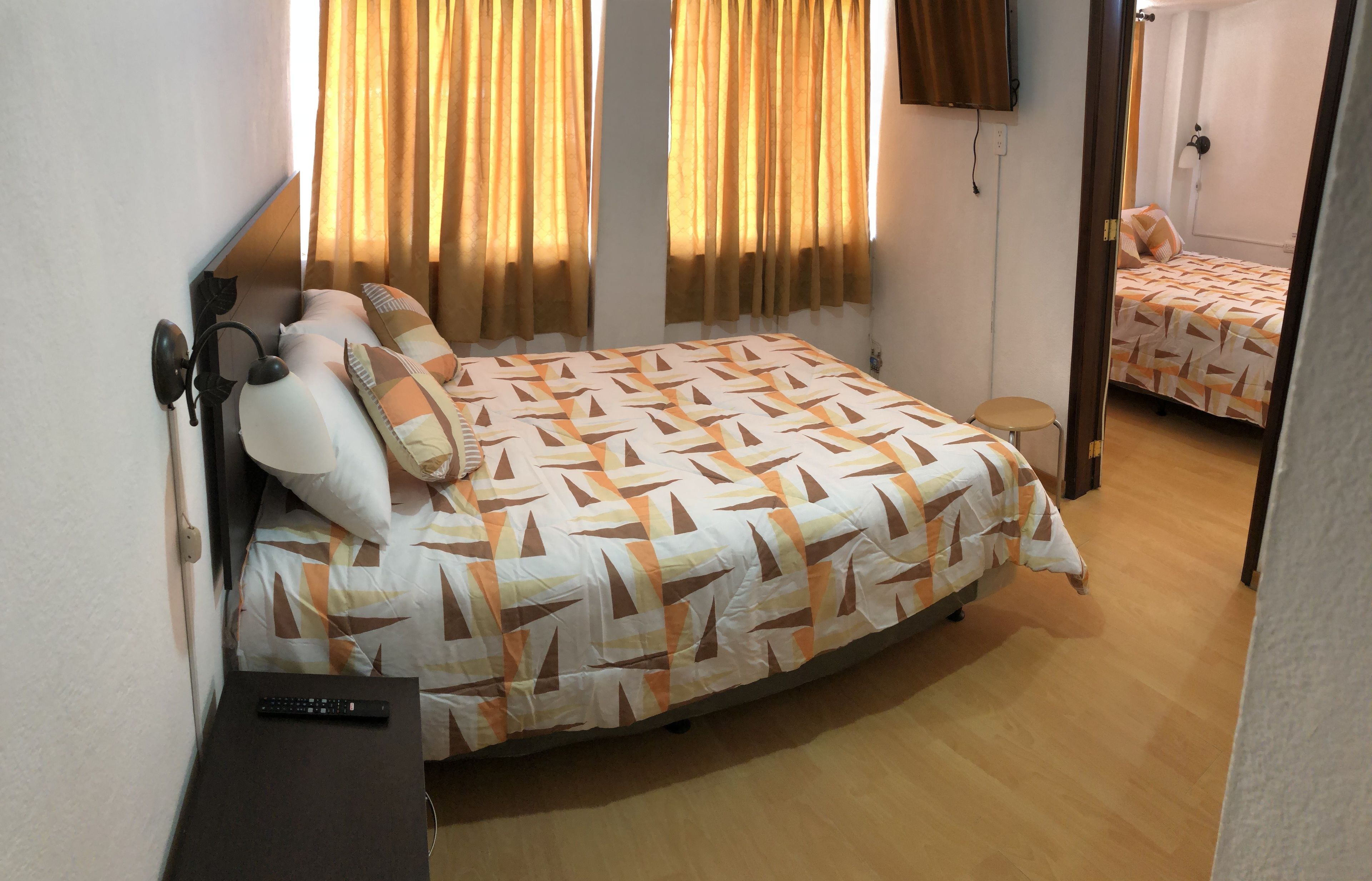 A bedroom with a bed, a nightstand, a remote control, and a mirror.