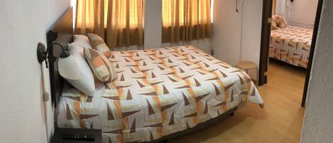 A bedroom with a bed, a nightstand, a remote control, and a mirror.
