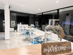 Un espace repas moderne agrémenté d’une pancarte « Bienvenue », de tables, de chaises et d’un centre de table décoratif constitué d’une bouteille en verre.