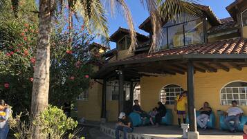 A building with a yellow facade, a tiled roof, and a covered porch with blue seating.