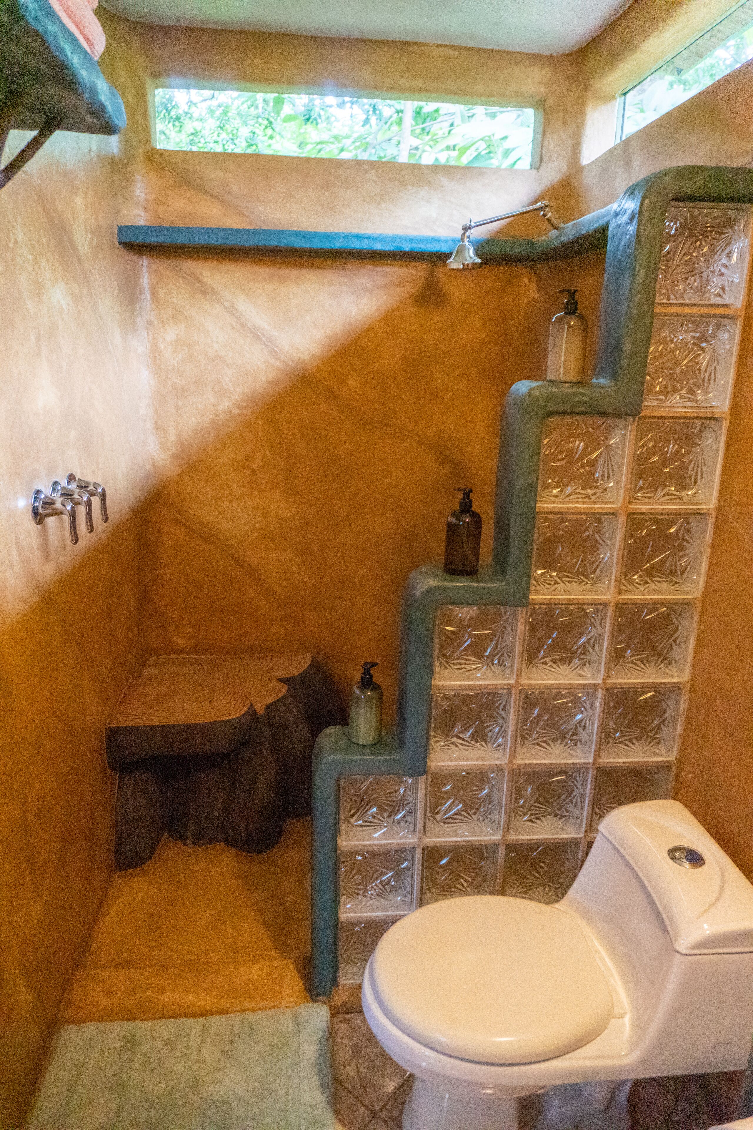 Ein Badezimmer mit einer hölzernen Sitzbank, Toilette und einer Duschkabine mit einer Glasbausteinwand.