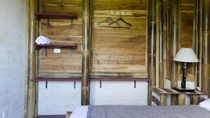 Une pièce en bois comprenant un lit, une table de chevet, une lampe, une étagère avec une serviette et deux cintres accrochés au mur.