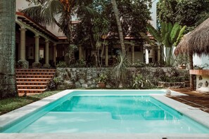 Una piscina con pared de piedra y plantas tropicales.