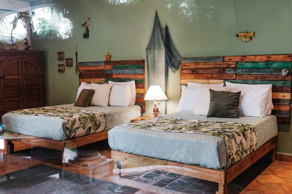 Une chambre avec deux lits, des têtes de lit en bois, une table de chevet avec une lampe et une décoration en forme d’étoile de mer au mur.