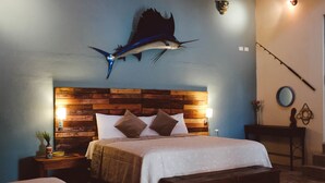 Un dormitorio con cabecera de madera, cama con ropa de cama blanca, mesita de noche con lámpara y una caña de pescar colgada en la pared.
