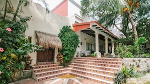 Un edificio con techo de paja, entrada, escalones de baldosas coloridas y un porche cubierto con columnas.