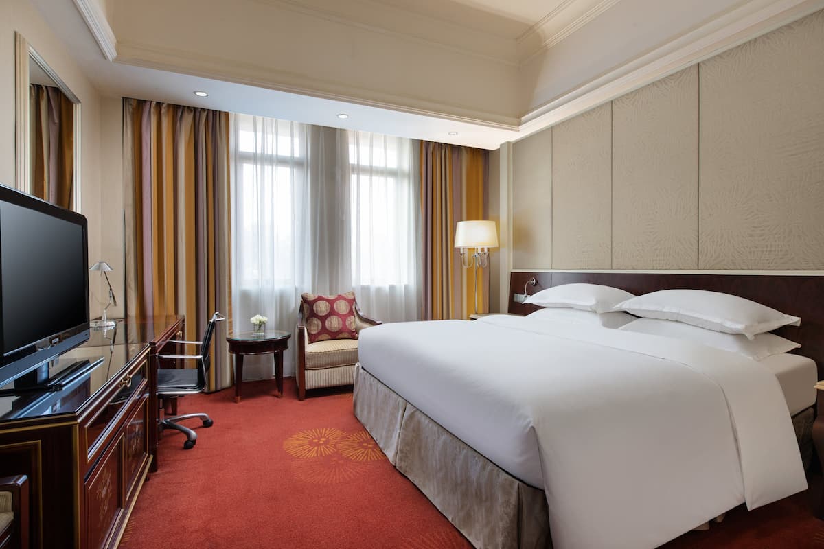 A hotel room with a large bed, a television, a desk, and a chair.