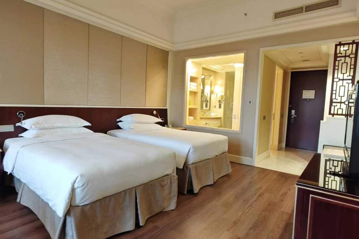 A hotel room with two beds, wooden flooring, a large mirror, and a door leading to a bathroom.