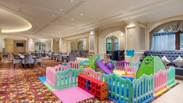 A hotel lobby with a children's play area, including a slide and soft play structures, and a seating area with tables and chairs.