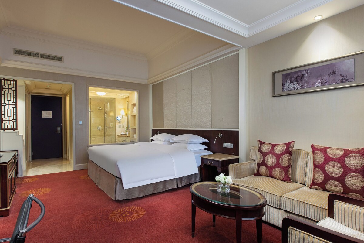Ein Hotelzimmer mit einem Bett, einer Couch, einem Fernseher, einem Schreibtisch und einem Badezimmer.