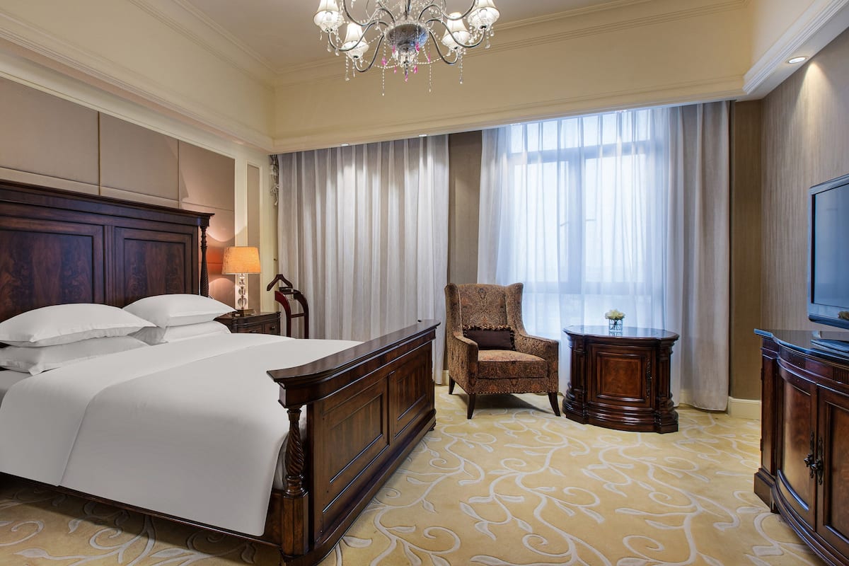 A hotel room with a large bed, a wooden nightstand, a chair, a desk, and a television.
