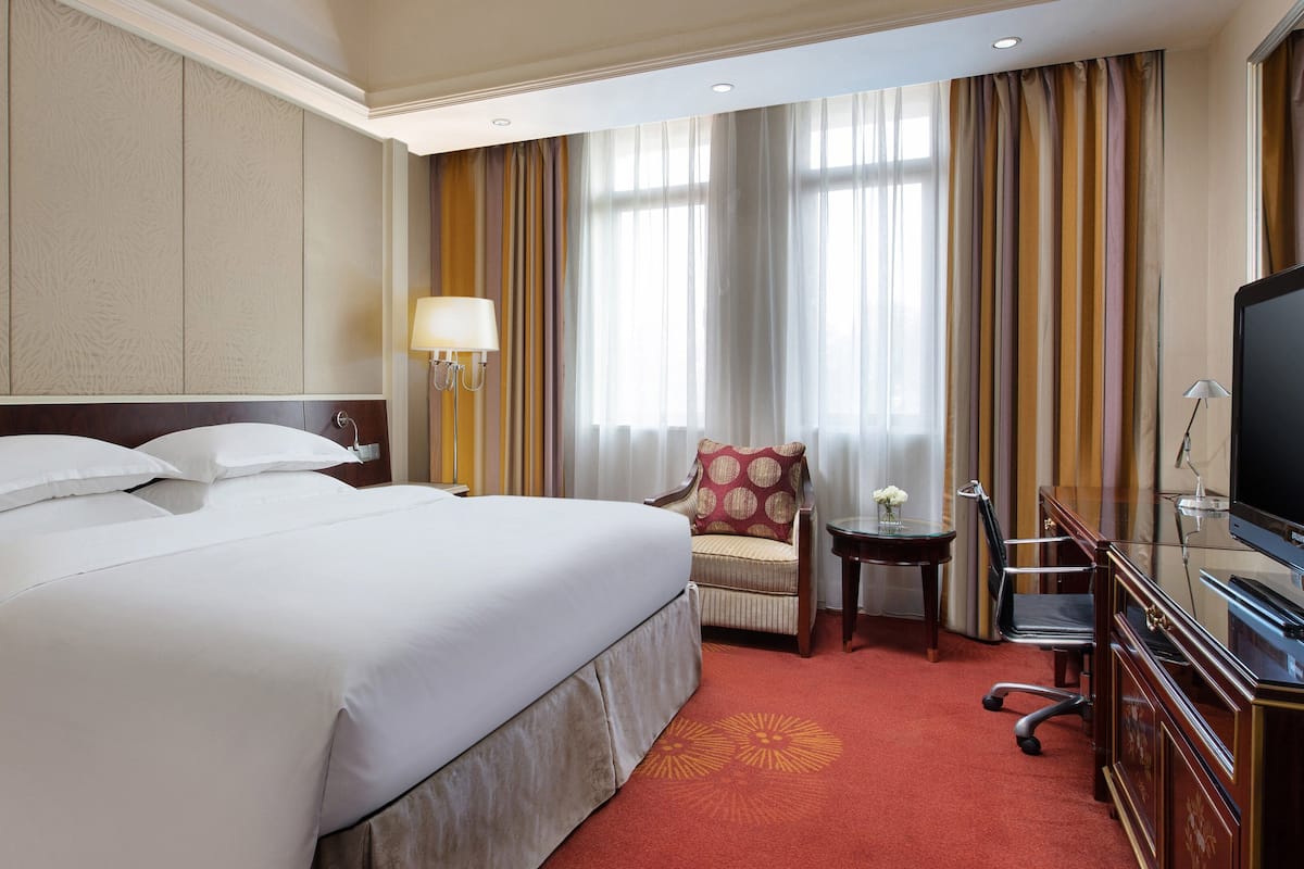 A hotel room with a large bed, a chair, a TV, and a small table.