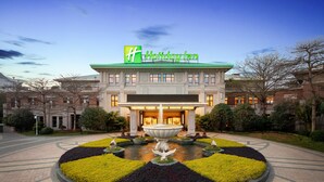A Holiday Inn hotel with a central fountain, surrounded by a landscaped garden with trimmed bushes and a paved walkway. - Holiday Inn Fuzhou New Port by IHG (Fuzhou)