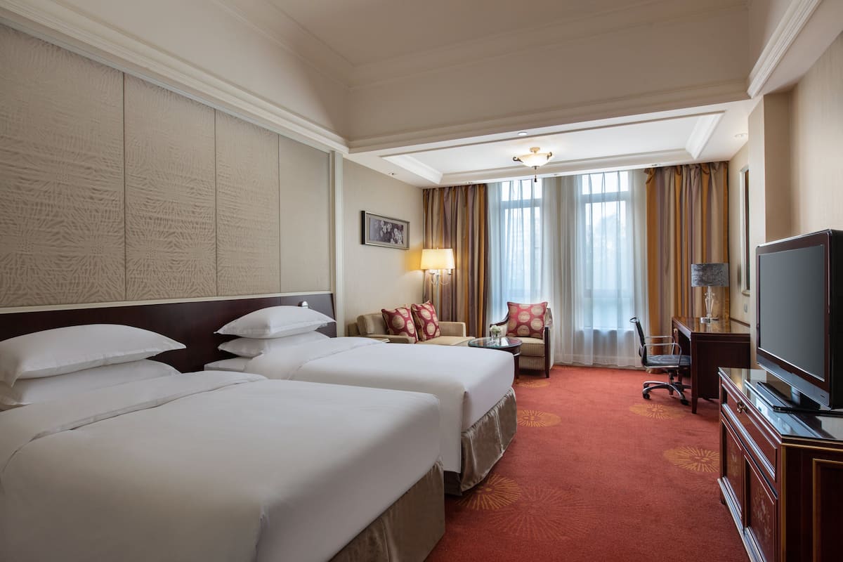 A hotel room with two beds, a desk, a chair, a television, and a window with curtains.