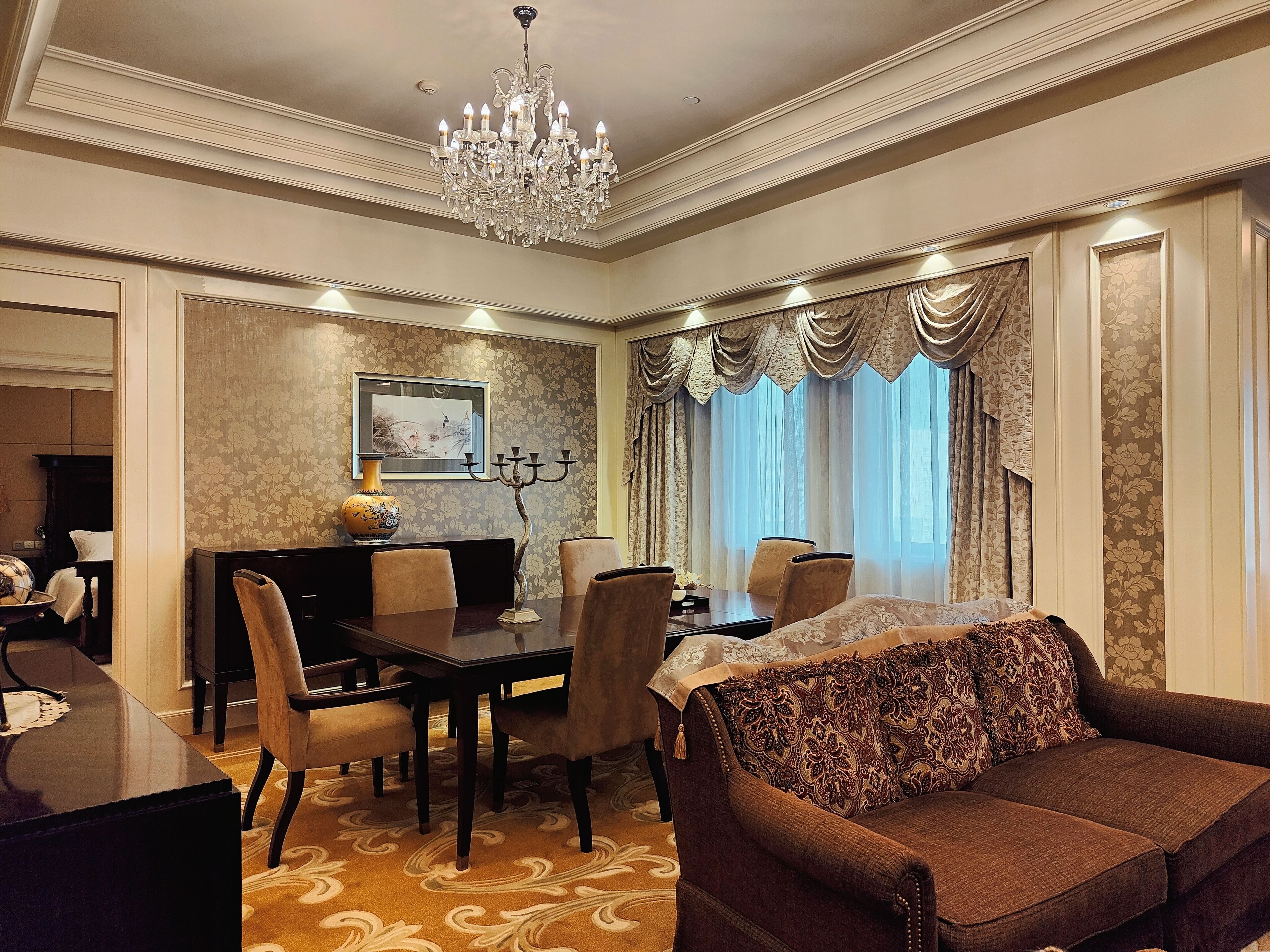 A dining area with a chandelier, a dining table, chairs, and a sofa.