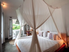 A bedroom with a canopy bed, a small table with a lamp, and a view of the outdoors. - Lila Boutik Canggu (Canggu)