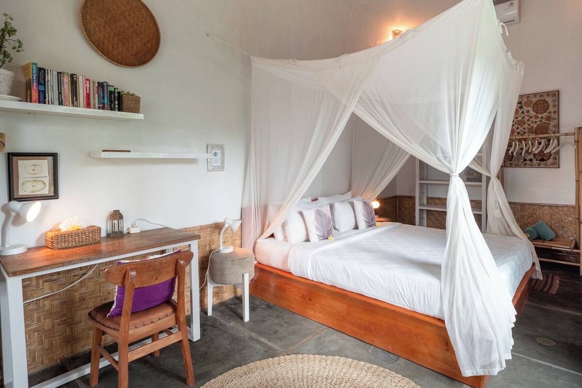 A bedroom with a wooden bed, white canopy, bedside tables, a desk, and a chair.