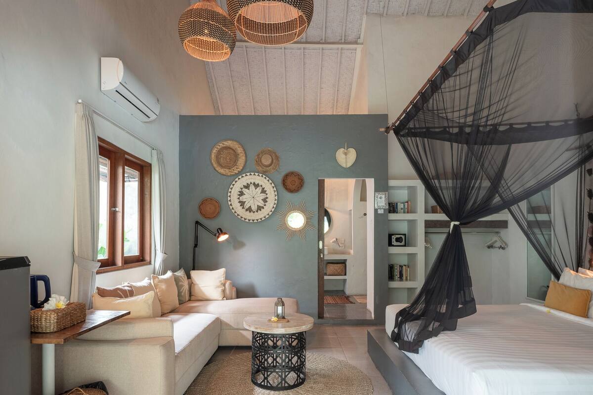 A bedroom with a bed, a sofa, a small round table, a wall with decorative plates, and a ceiling fan.