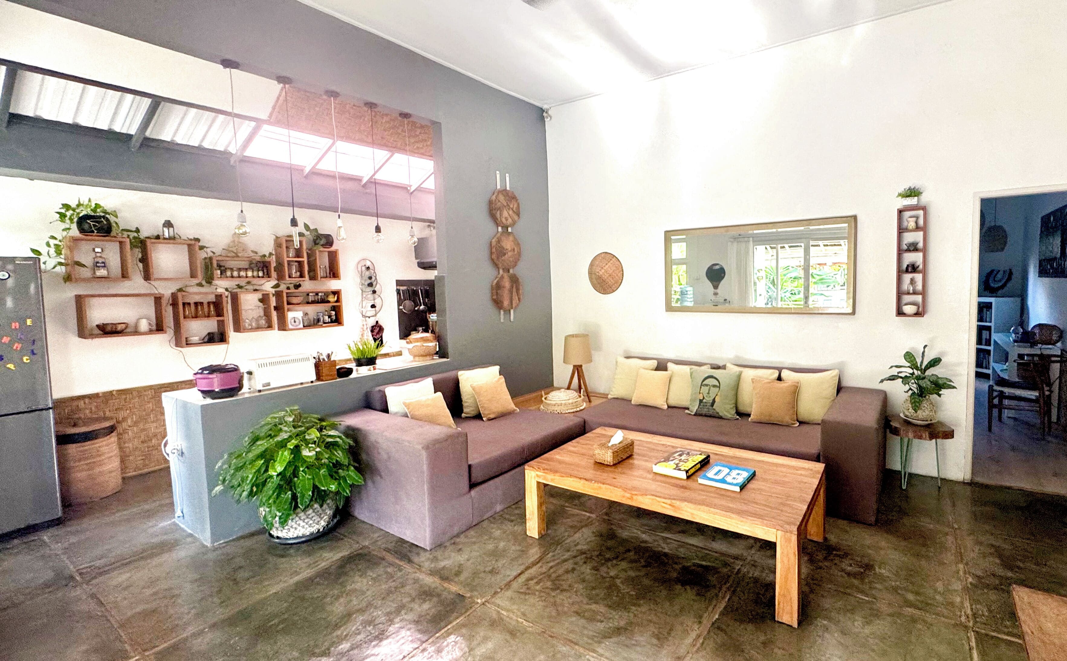 A modern living room with a sofa set, a coffee table, and a kitchen area with shelves and plants.