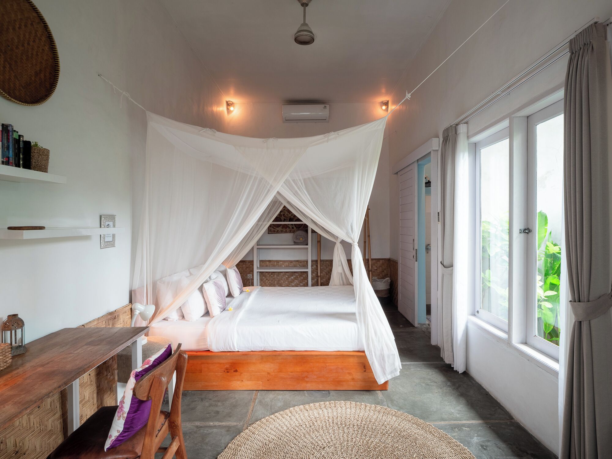 Une chambre avec un lit à baldaquin, un bureau en bois et une vue sur la verdure.