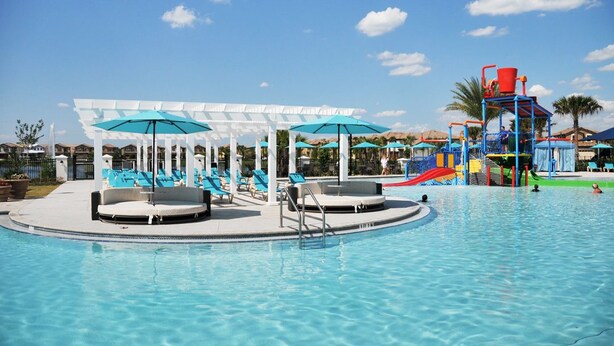 Une piscine avec des chaises longues et des parasols, un espace de jeux aquatiques et un coin salon abrité.